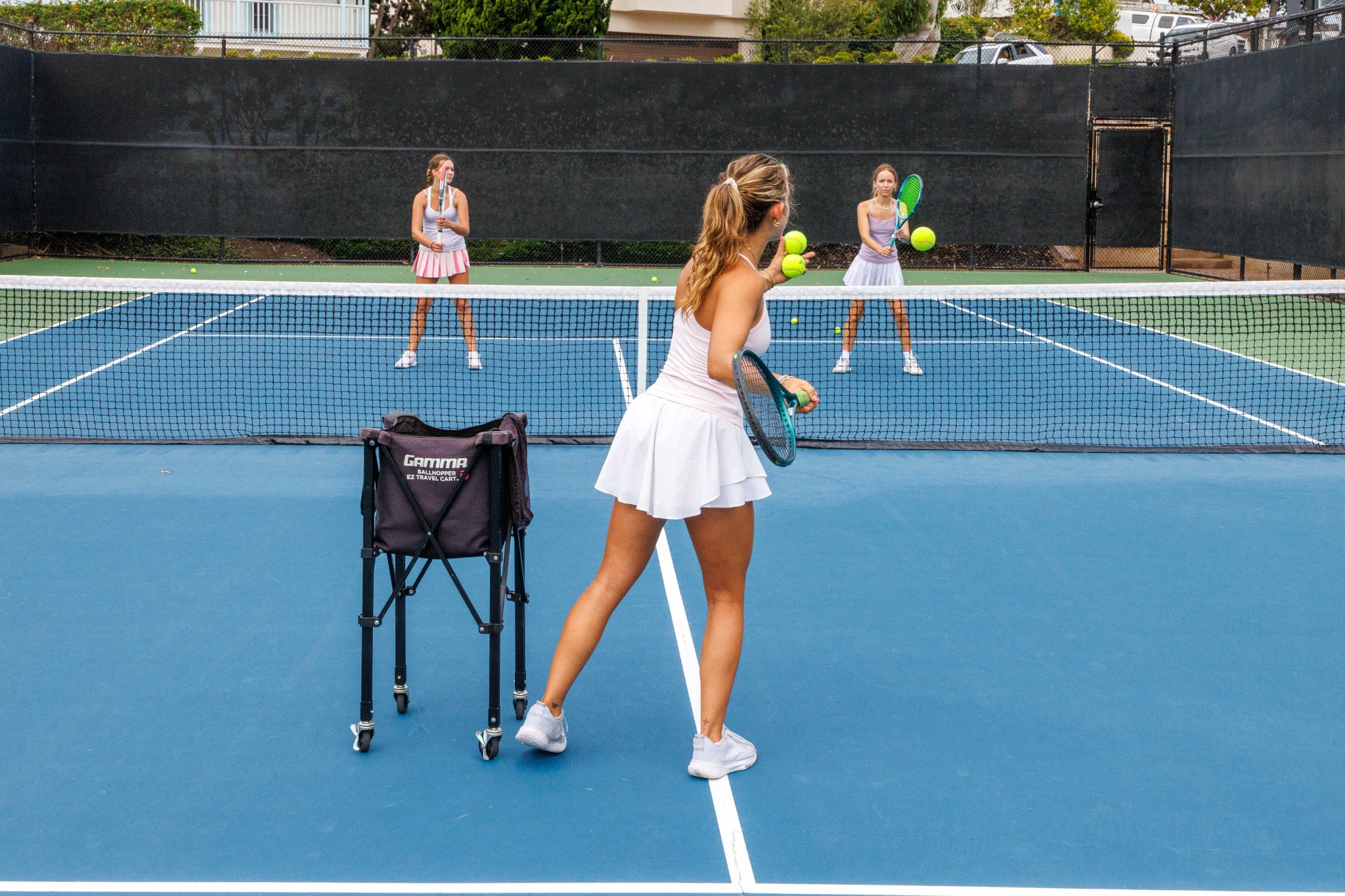 DB Tennis coach feeding balls to junior players